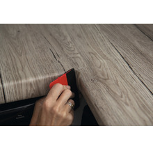 Person verwendet Werkzeug zum Anbringen von selbstklebender Holzdekorfolie