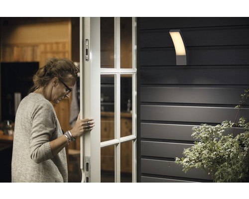 Eine Frau öffnet eine Tür neben einer Aussenleuchte an einer Hauswand