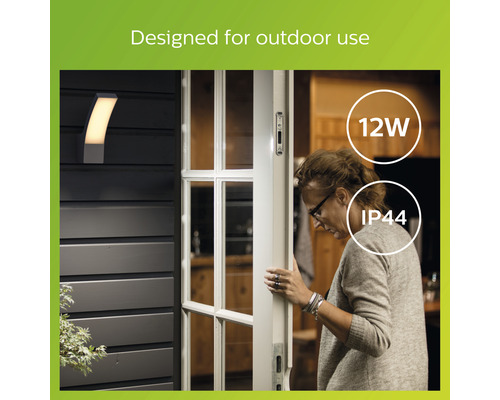 Eine Außenwandleuchte neben einer Haustür, die eine Frau öffnet, gekennzeichnet mit 12 Watt und IP44 Schutzart.