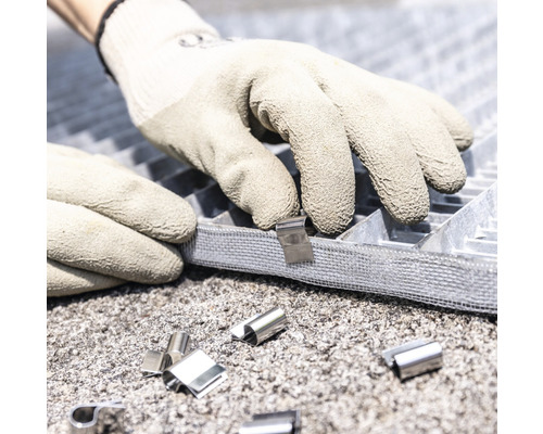 Hände mit Arbeitshandschuhen befestigen eine Metallschiene an einem Gitterrost.