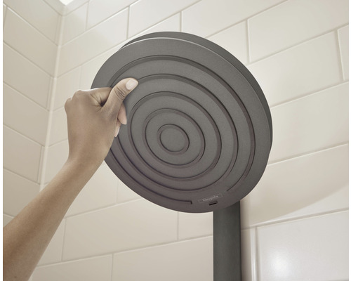 Hand berührt einen runden Duschkopf im Badezimmer