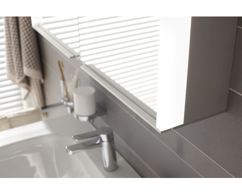 Detailaufnahme eines Badezimmerspiegelschranks mit Beleuchtung über einem Waschbecken mit Armatur