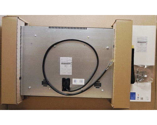 Rückansicht eines Kochfeldes mit Anschlusskabel und Montagezubehör in einer Verpackung