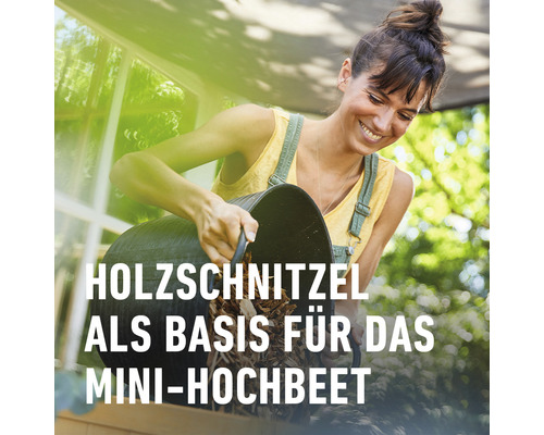Frau befüllt Mini-Hochbeet mit Holzschnitzeln
