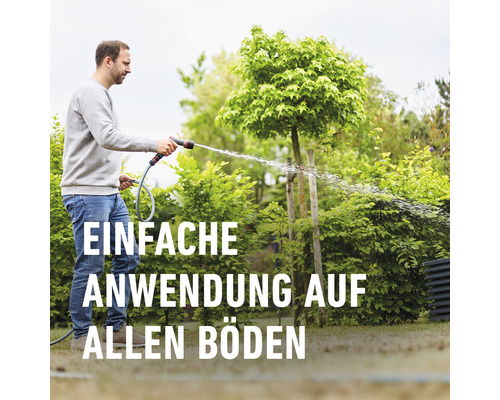Ein Mann bewässert mit einem Gartenschlauch und einer Spritzpistole den Garten.