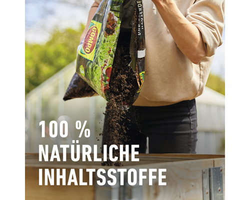 Eine Person schüttet Blumenerde aus einer Tüte in ein Beet.