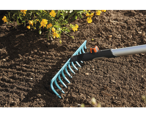 Gartenrechen im Einsatz auf einem Beet mit Erde und gelben Blüten