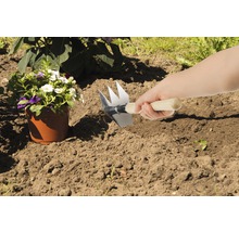 Szene mit einer Person, die ein Beet mit einer Gartenkralle vorbereitet, neben einem Blumentopf.