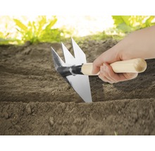 Nahaufnahme einer Hand, die eine Gartenhacke mit Holzgriff in die Erde steckt