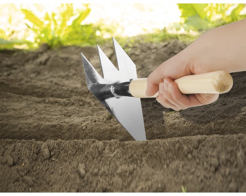 Nahaufnahme einer Hand, die eine Gartenhacke mit Holzgriff in die Erde steckt