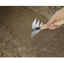 Nahaufnahme einer Person, die eine Pendelhacke mit Holzgriff im Garten verwendet.