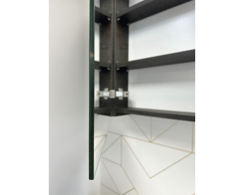 Detailaufnahme eines Spiegelschranks mit Glasablage und dunklem Holzrahmen an einer weißen Wand mit Fliesenmuster