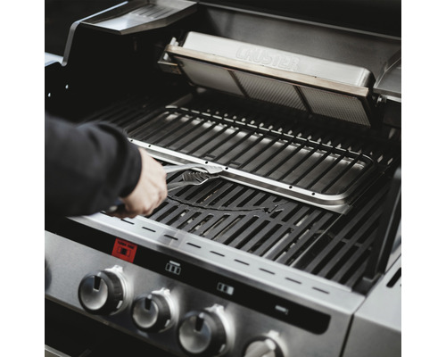 Person hantiert mit einer Grillzange an einem Gasgrill. Zu sehen sind Grillrost und Brenner.