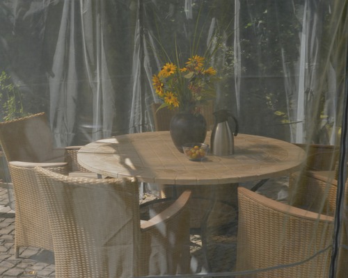 Runder Gartentisch mit Stühlen und Dekoration unter einer transparenten Abdeckung.