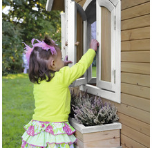 Ein Kind öffnet ein Fenster an einem Holzspielhaus mit Blumenkasten.