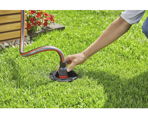 Eine Person schliesst einen Gartenschlauch an einen Wasseranschluss im Garten an