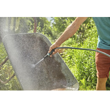 Eine Person reinigt eine Schubkarre mit einem Wasserschlauch im Garten.