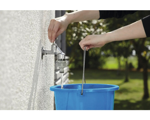 Eine Person befüllt einen blauen Eimer mit Wasser aus einem Wasserhahn im Freien.