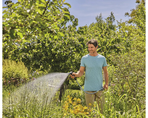 Mann bewässert Garten mit Gartenschlauch und Sprühdüse
