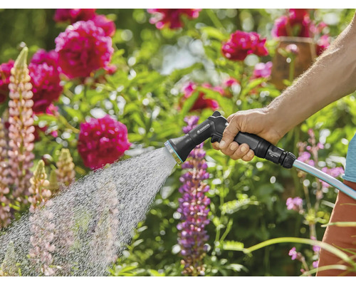 Eine Person bewässert mit einer Gartenspritze einen Garten.