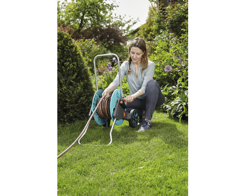 Eine Frau benutzt einen Gartenschlauchwagen im Garten.