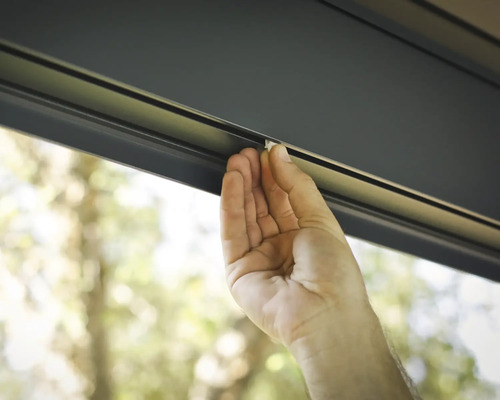 Eine Hand befestigt einen weißen Halter in einer dunklen Schiene.