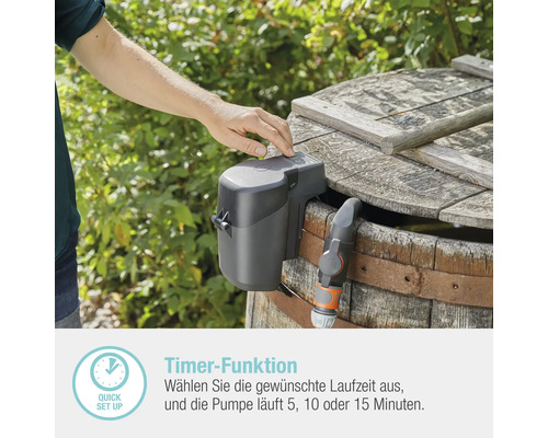 Eine Person bedient eine Regenfasspumpe mit Timer-Funktion an einem Holzfass