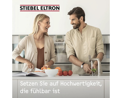 Frau schneidet Gemüse neben einem Mann, der Gemüse wäscht, Stiebel Eltron Logo