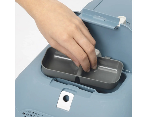 Nahaufnahme einer Hand, die eine graue Auffangschale in eine blaue Katzentoilette einsetzt