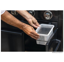 Person setzt eine Wasserschale in einen Gasgrill.