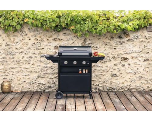 Drei-Brenner-Gasgrill auf einer Holzterrasse vor einer Steinmauer mit Pflanzen.