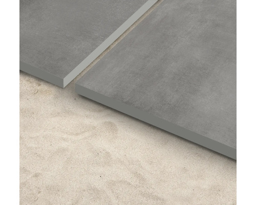 Graue Bodenfliesen auf sandigem Untergrund.