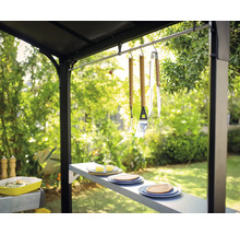 Grillszene im Freien mit Grillbesteck, Geschirr und Beilagen unter einem Grillpavillon.