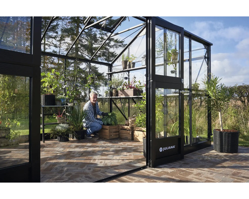 Geräumiges Gewächshaus mit Pflanzen und einem Mann, der im Garten arbeitet.