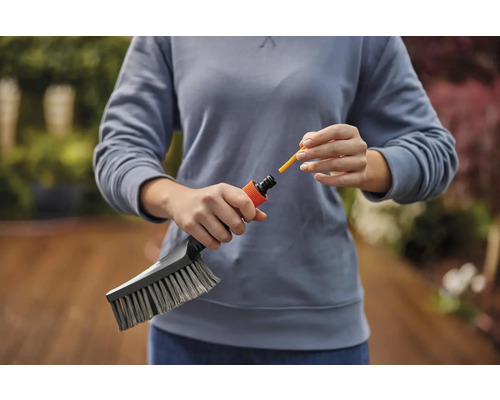 Eine Person befestigt eine gelbe Düse an einer Bürste für die Gartenreinigung.