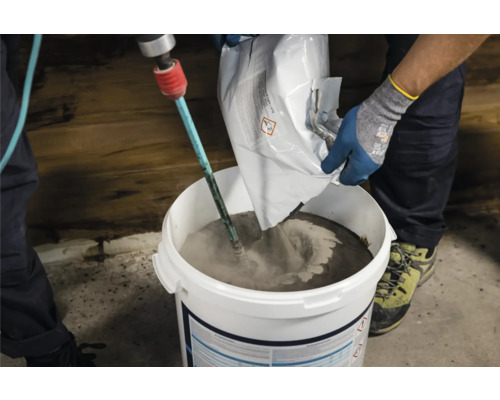 Handwerker mischt Mörtel mit einem Rührgerät in einem Eimer.