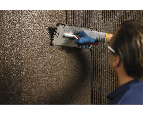 Handwerker trägt Fliesenkleber mit einer Glättkelle auf eine Wand auf.