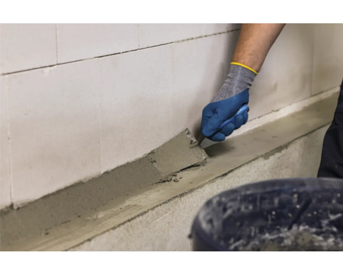 Handwerker trägt Mörtel mit einer Kelle auf eine Wand auf