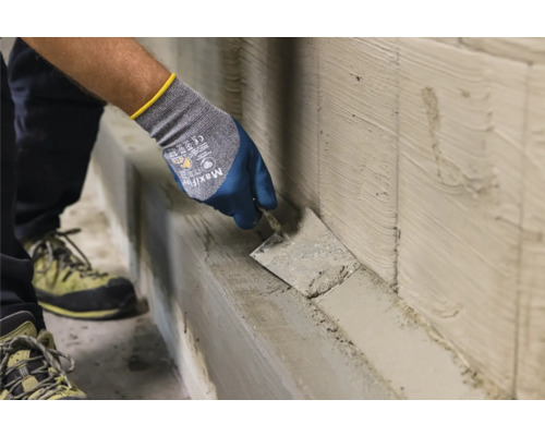 Eine Person trägt mit einer Maurerkelle Putz auf eine Wand auf.