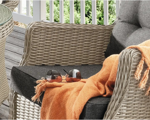 Detailansicht eines Korbsessels mit Kissen, einer Decke und einer Sonnenbrille auf einer Terrasse