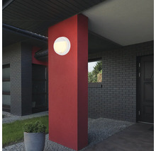 Runde Außenleuchte an roter Säule vor einem Haus.