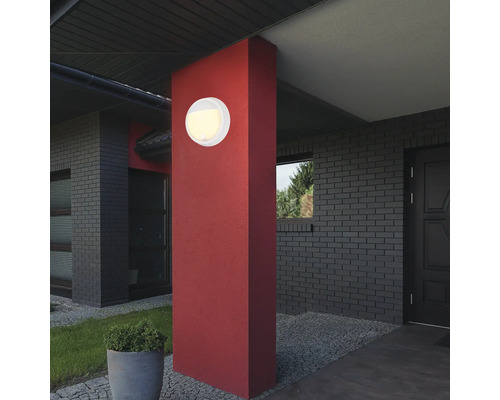 Runde Außenleuchte an roter Säule vor einem Haus.