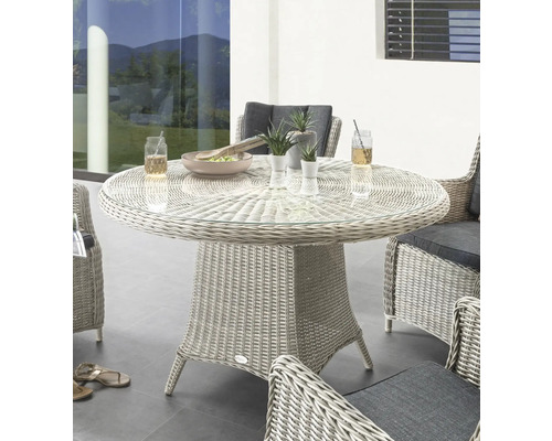 Runder Gartentisch mit Glasplatte und Rattansockel, umgeben von Rattansesseln mit grauen Kissen.