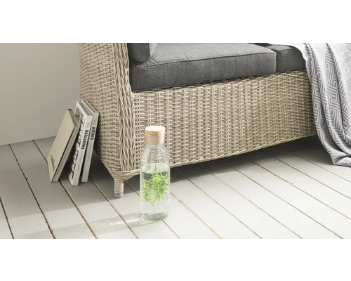 Nahaufnahme eines Korbsessels mit Kissen, Flasche mit Wasser und Pflanzen sowie einigen Büchern