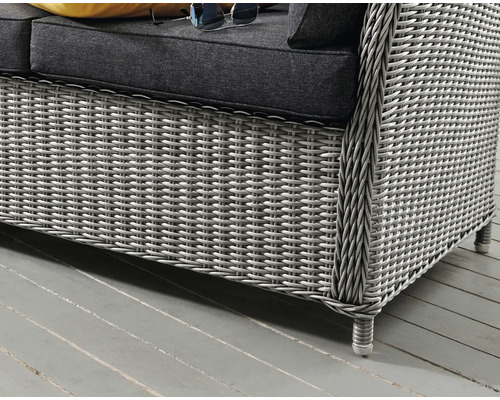 Detailansicht eines grauen Rattan-Gartensofas mit Kissen und Sonnenbrille