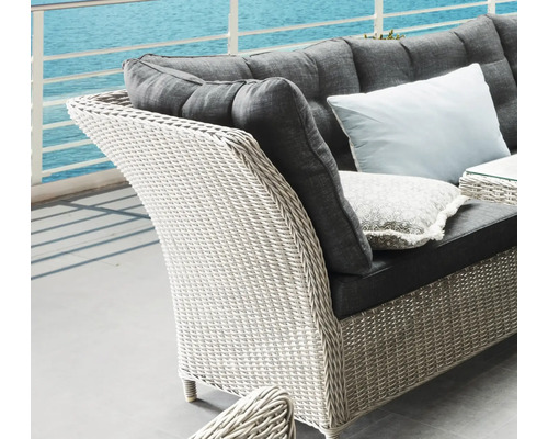 Detailansicht eines Korbsessels mit Polster und Kissen vor einem Meer.