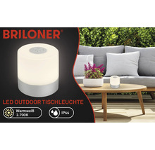 Briloner Logo. LED-Tischleuchte für den Außenbereich auf einem Tisch im Garten.