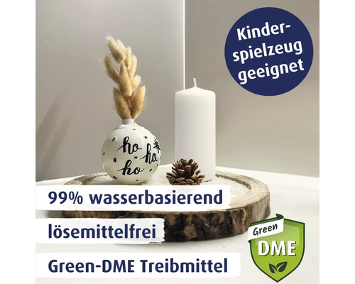 Dekorative Anordnung mit Weihnachtskugel, Kerze und Tannenzapfen auf Holzscheibe, mit Hinweisen zu 99 Prozent wasserbasiert, lösungsmittelfrei, Green-DME Treibmittel und Kinderspielzeug geeignet sowie Green DME Logo.