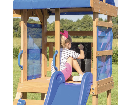 Mädchen malt auf einer Tafel auf einem Spielplatz aus Holz mit Rutsche und blauer Markise.