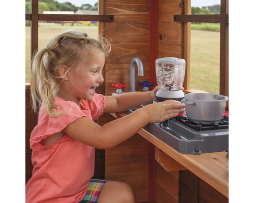 Ein Mädchen spielt in einer Holzküche mit Spielzeug-Mixer und Topf.